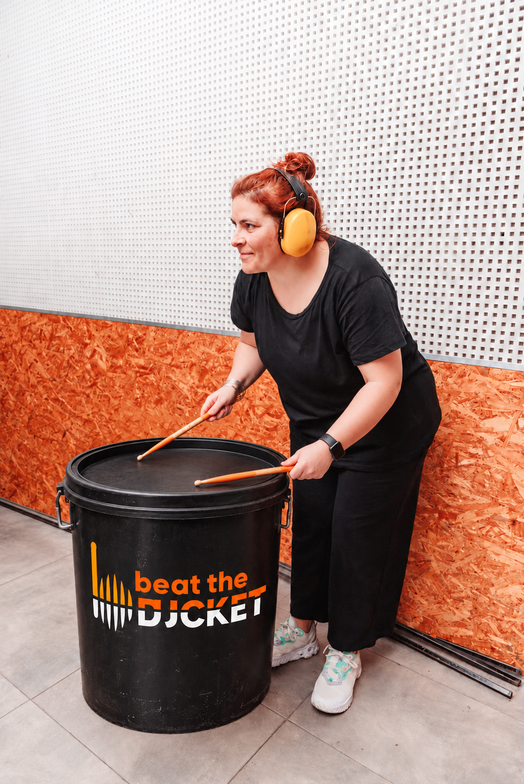 A participant wearing hearing protection and playing a branded bucket with drumsticks.
